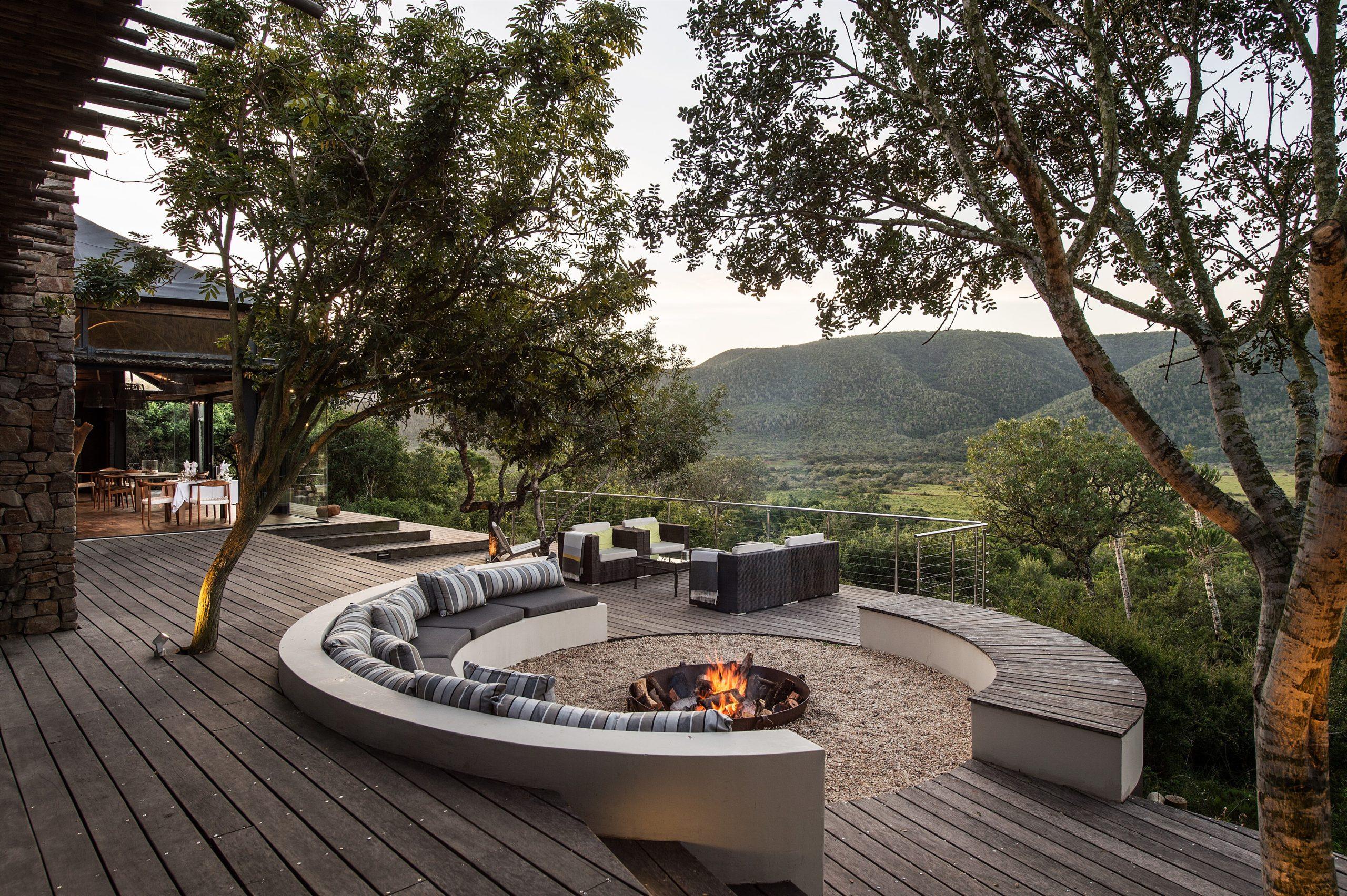 Outdoor lodge deck with a fire pit and seating overlooking a scenic valley at sunset.